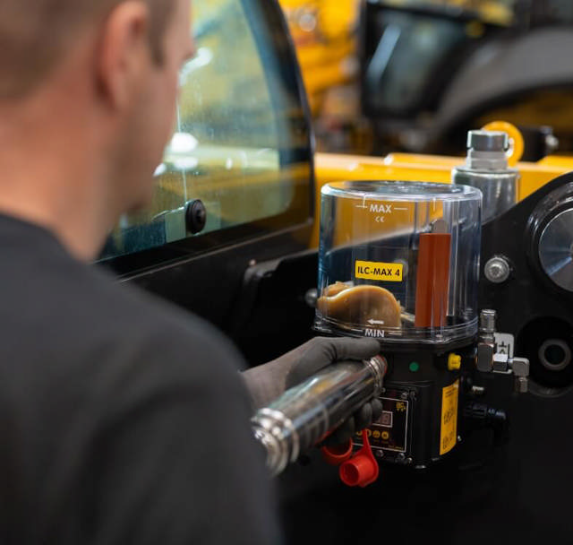 Montør fylder centralsmøringspumpe med fedt efter at have tjekket om alle slanger sidder korrekt